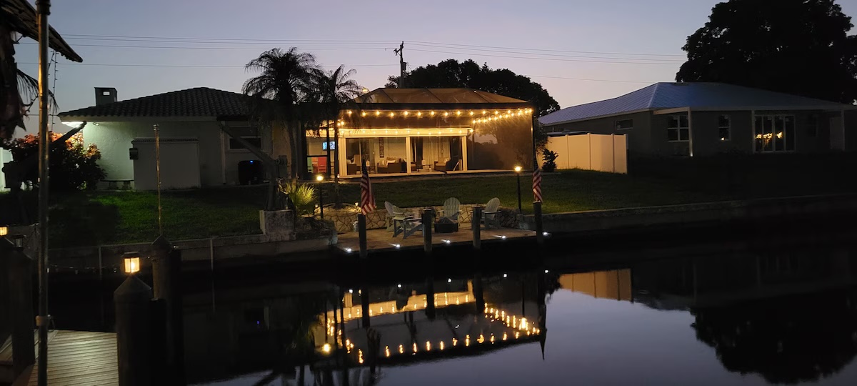 Home lit up at night from across the canal with string lights glowing over the screened patio