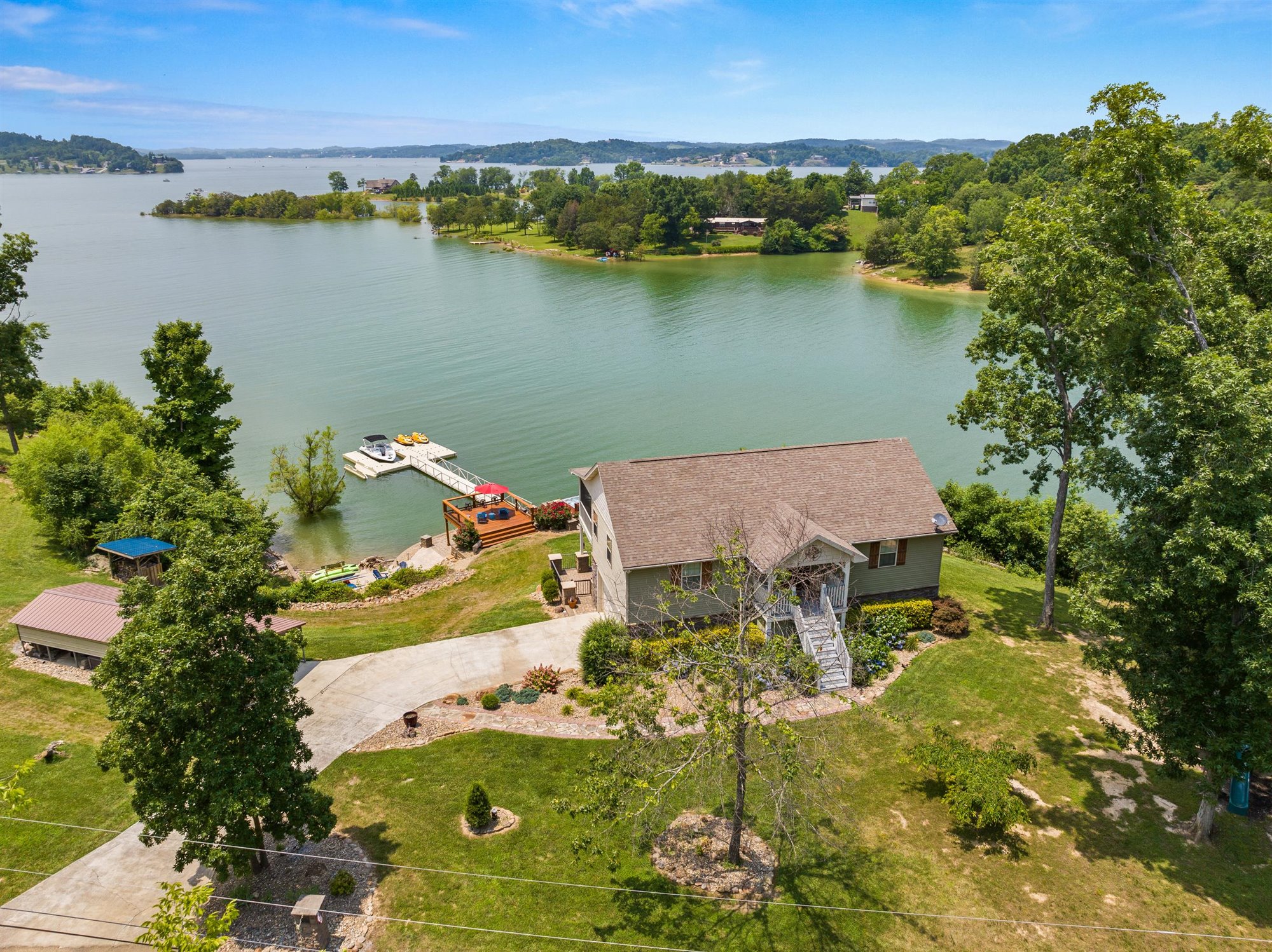 Aerial drone view of Fort Sunsets property showing the full house, lakeside patio with covered area, floating dock with watercraft, and expansive Douglas Lake stretching to distant hills