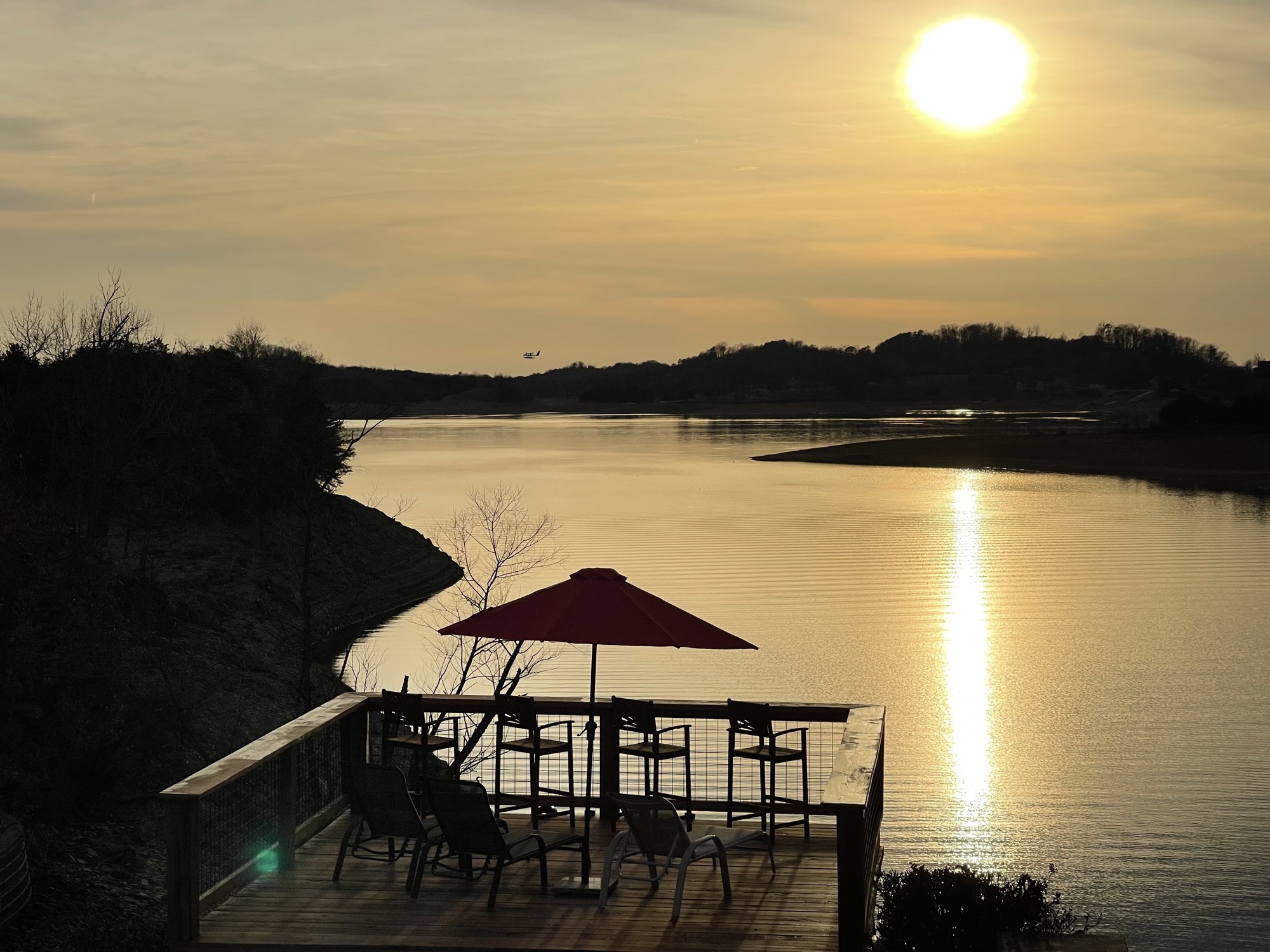 Red umbrella and bar stools silhouetted on the sundeck at sunset over Douglas Lake