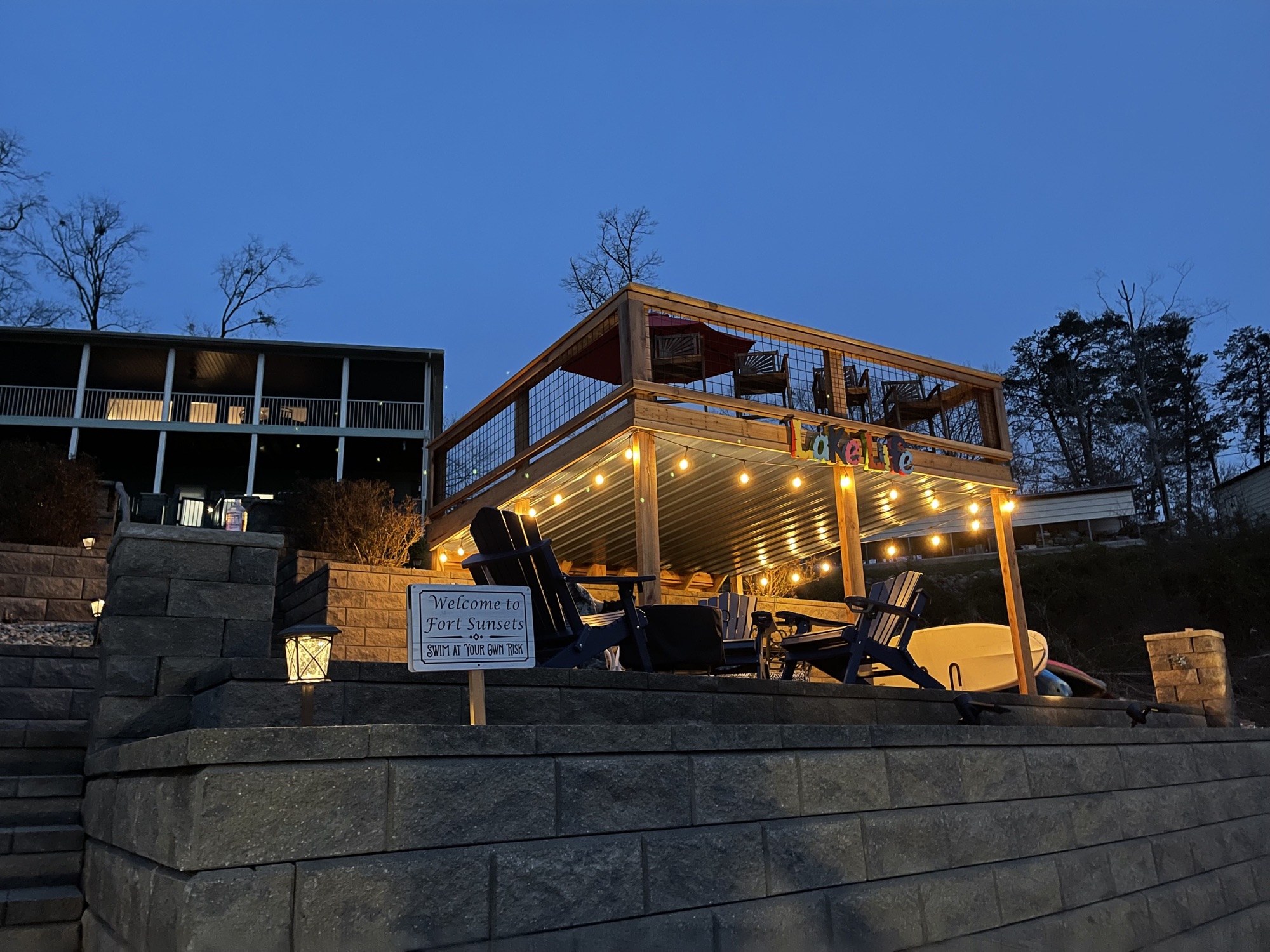Firepit pavilion glowing with string lights at night beside the Welcome to Fort Sunsets sign
