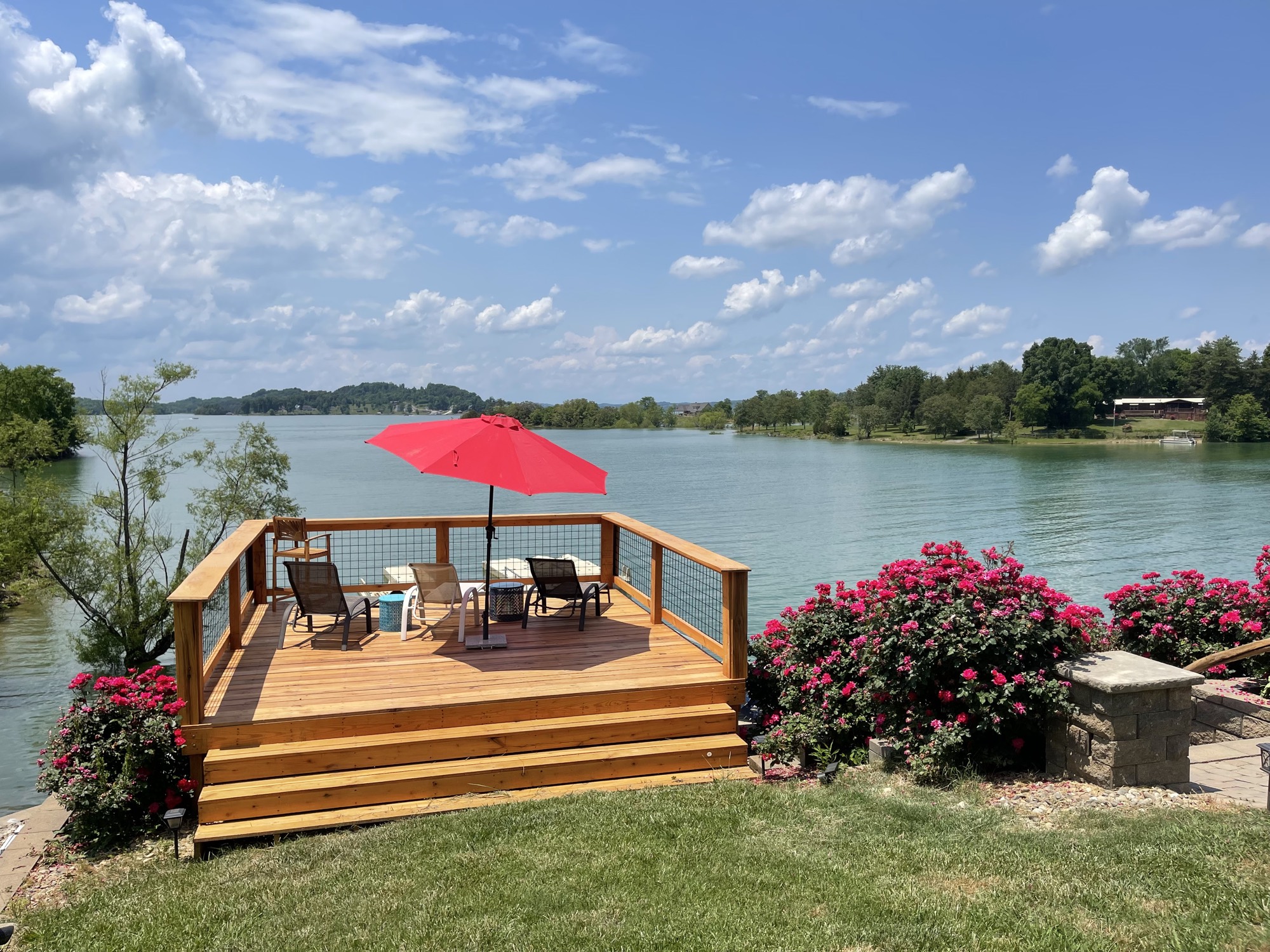 Sundeck with red umbrella surrounded by blooming rose bushes at the lake's edge