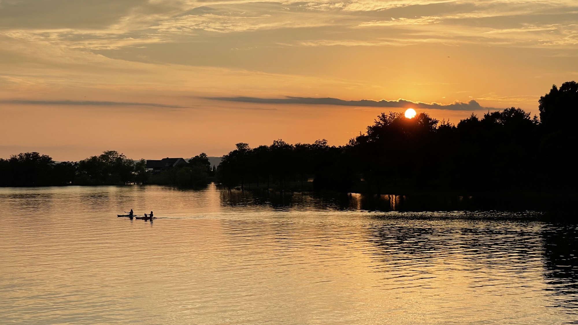 Two kayakers paddling across Douglas Lake as the sun sets behind the treeline